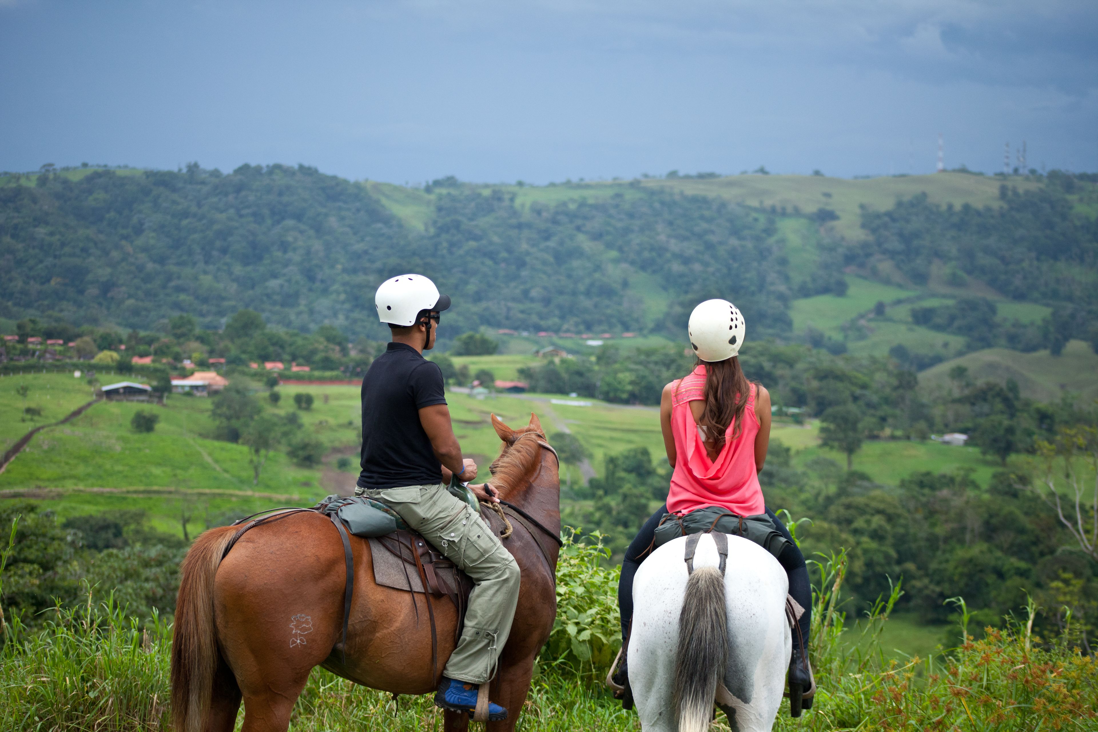Two people on horseback overlooking a hilly landscape.