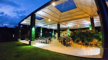 Un patio cubierto al aire libre con mesas y sillas, rodeado de vegetación.