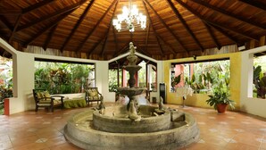 A covered patio with a central fountain, wooden furniture, and potted plants.