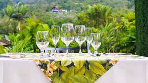 A table set with glasses and a tropical tablecloth, overlooking a mountain and lush greenery.