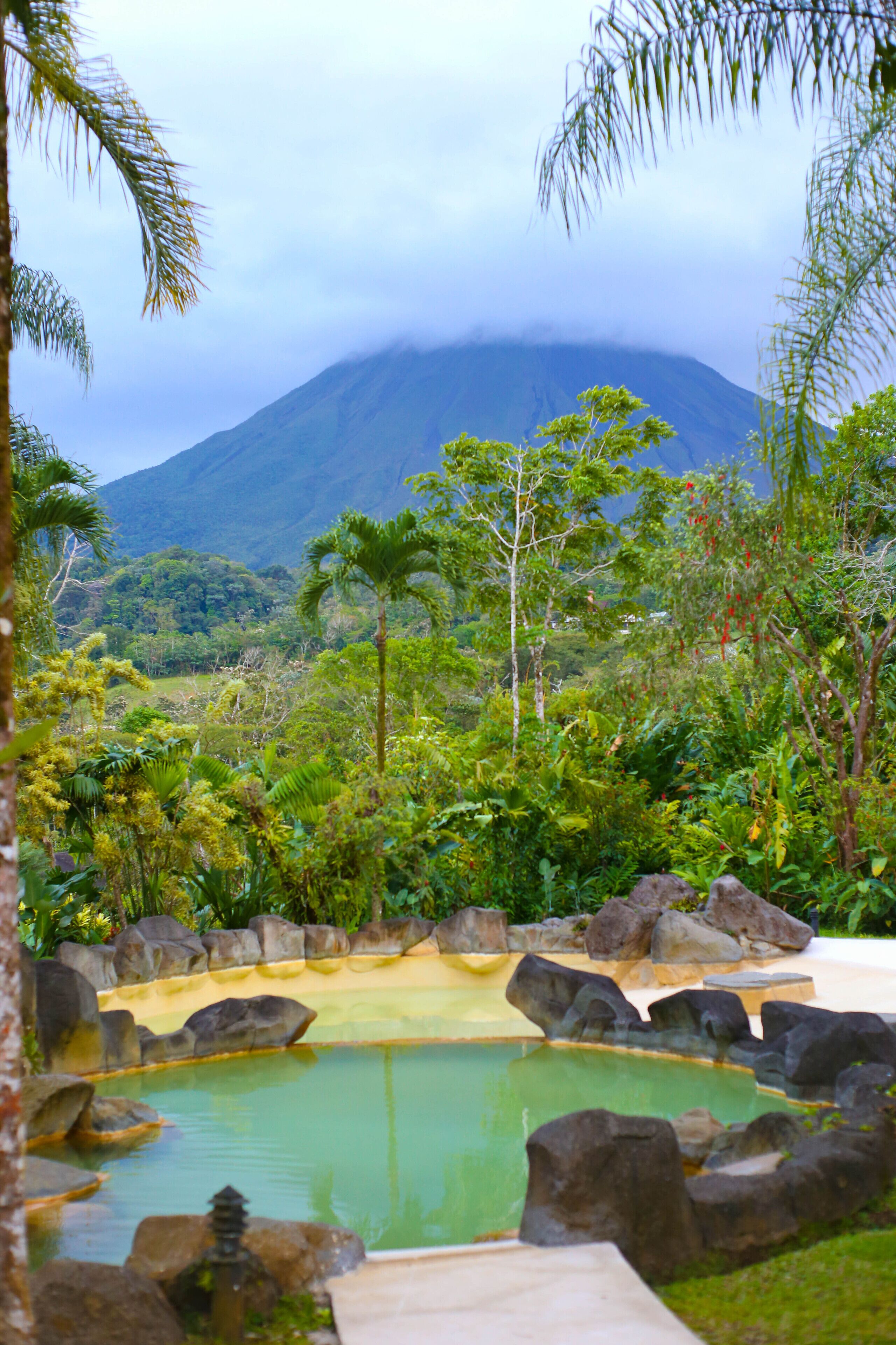 Un área de piscina tranquila rodeada de exuberante vegetación y rocas, con una montaña al fondo.