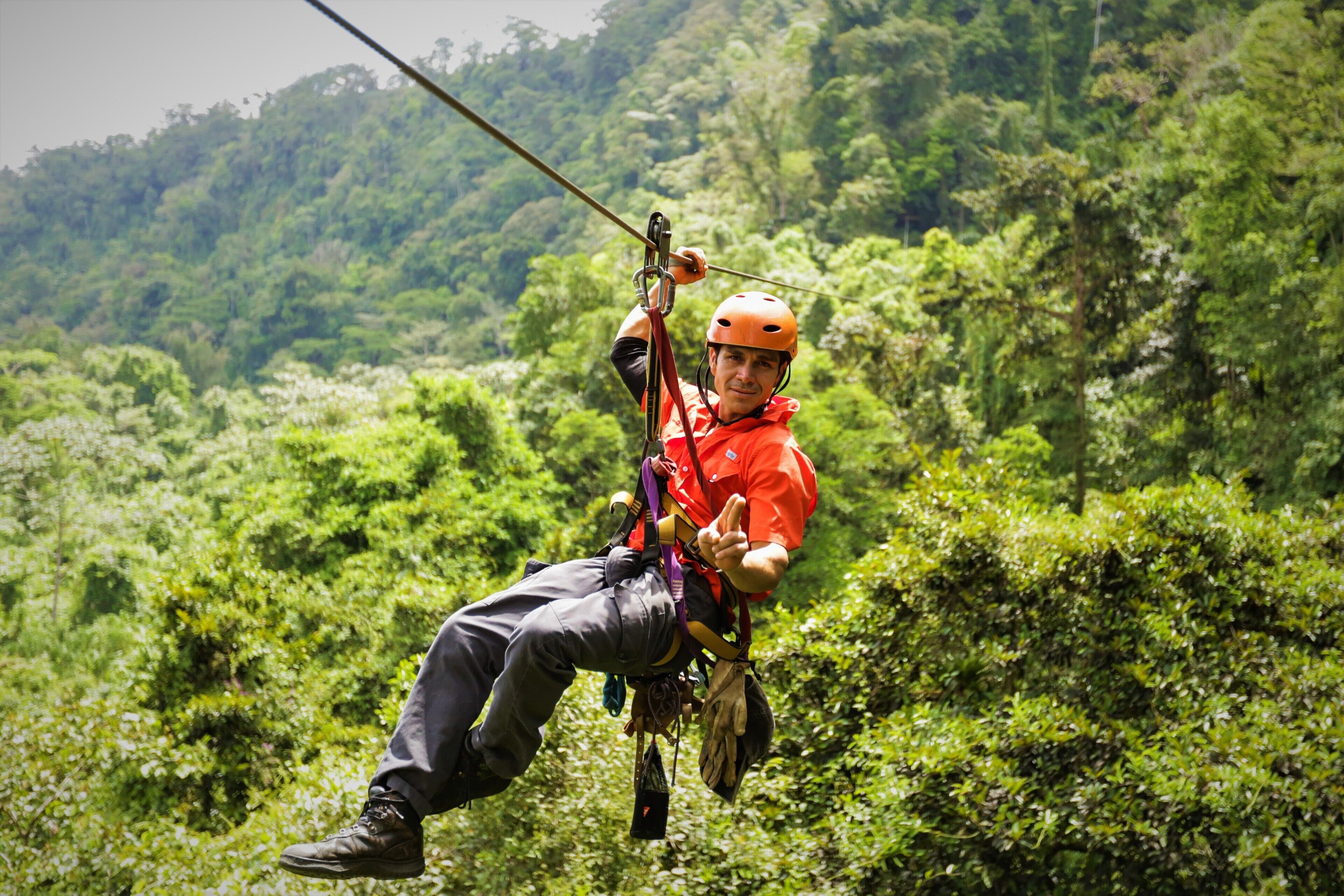 A person in a red shirt and helmet engaged in zip-lining through a forested area.