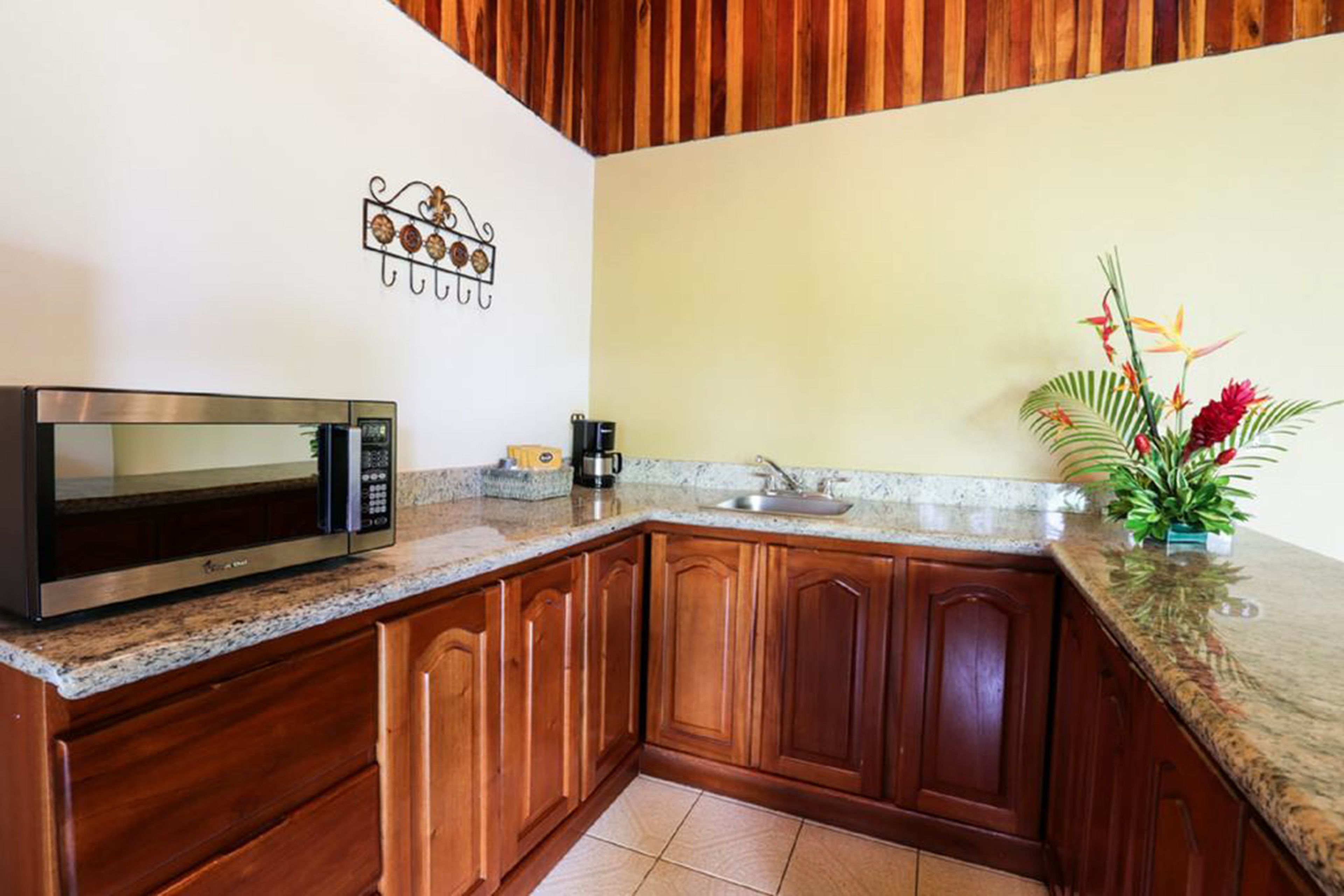 Cocina con armarios de madera, encimera de granito, microondas, cafetera y un adorno de pared.