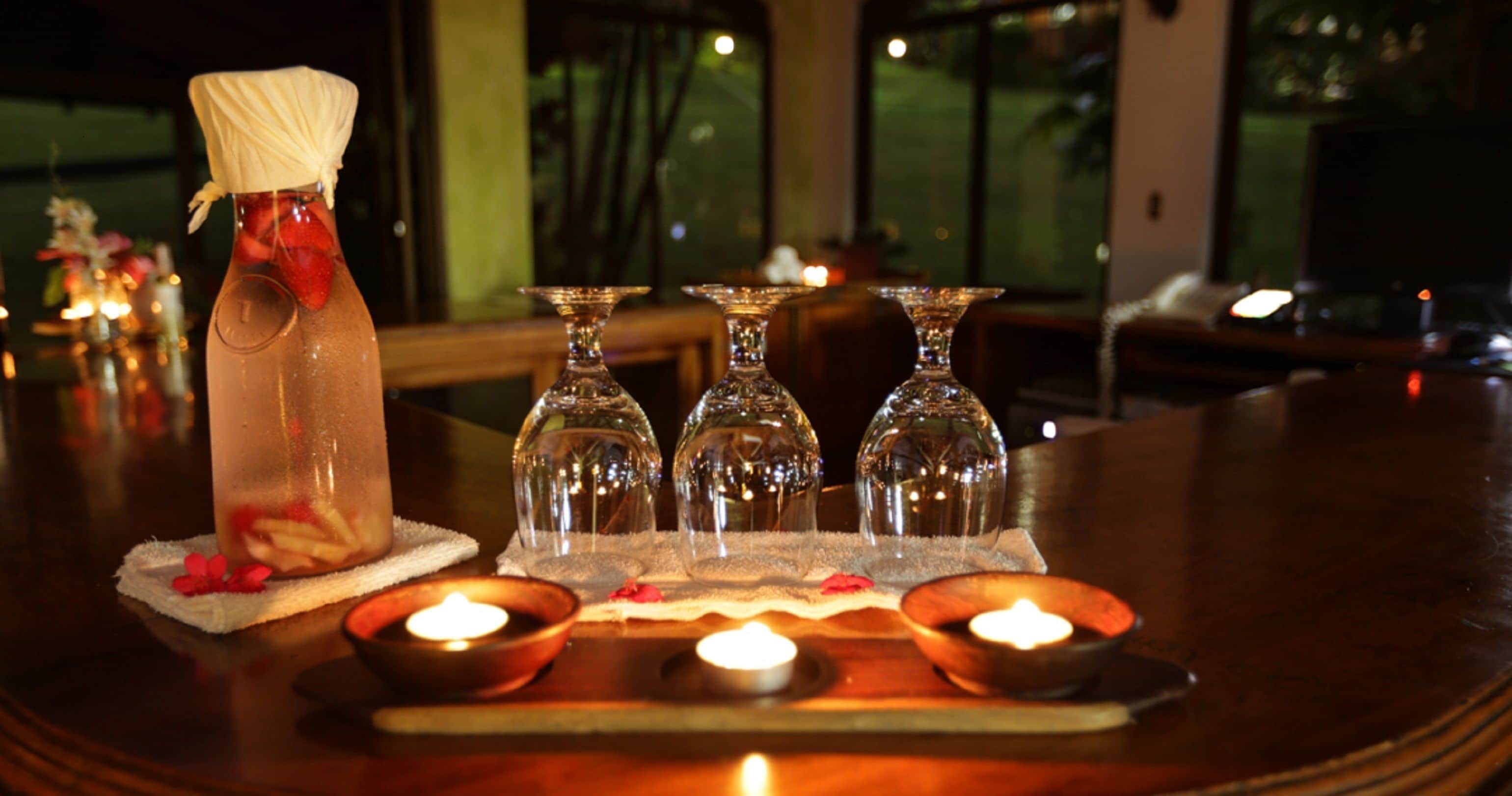 A table with a bottle of water, three glasses, and candles.