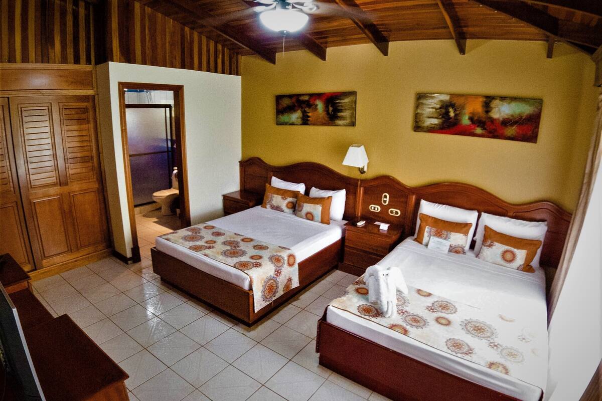 A hotel room with two beds, wooden headboards, a tiled floor, and a wooden ceiling.