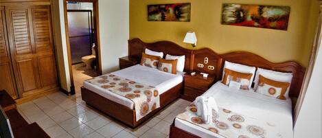A hotel room with two beds, wooden headboards, a tiled floor, and a wooden ceiling.