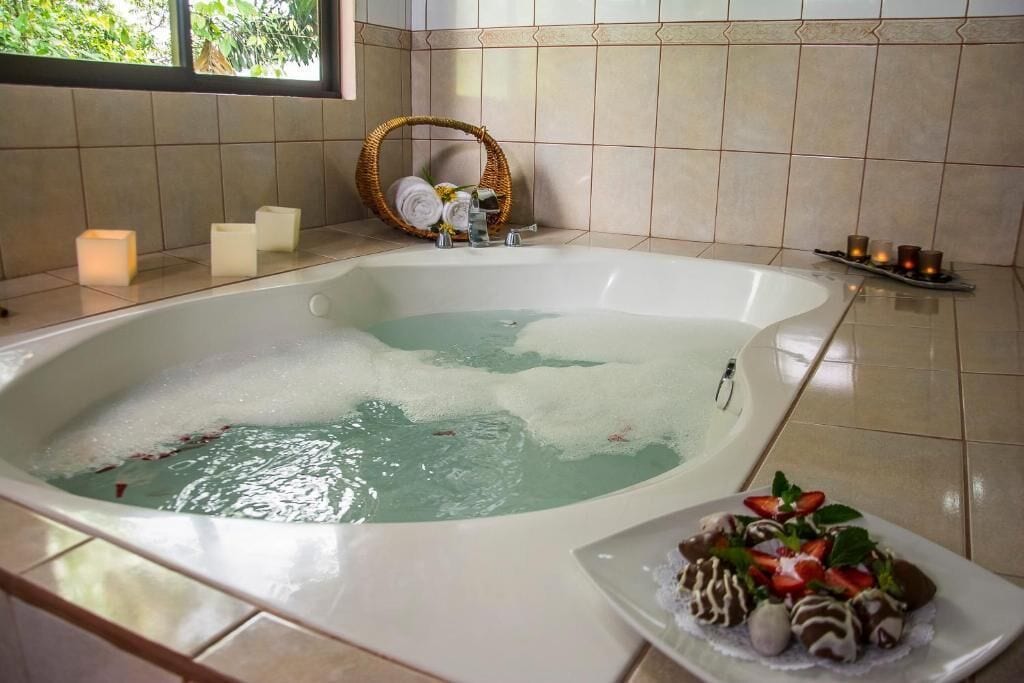 Une salle de bain avec une grande baignoire, un panier en osier rempli de serviettes et de bougies, ainsi qu’un plateau de fraises enrobées de chocolat.