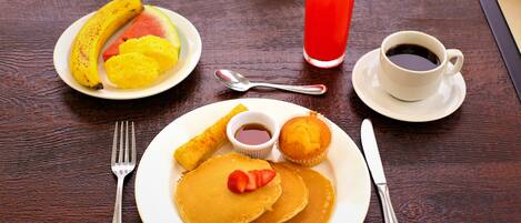 A breakfast setting with pancakes, fruit, a muffin, and a cup of coffee on a wooden table.