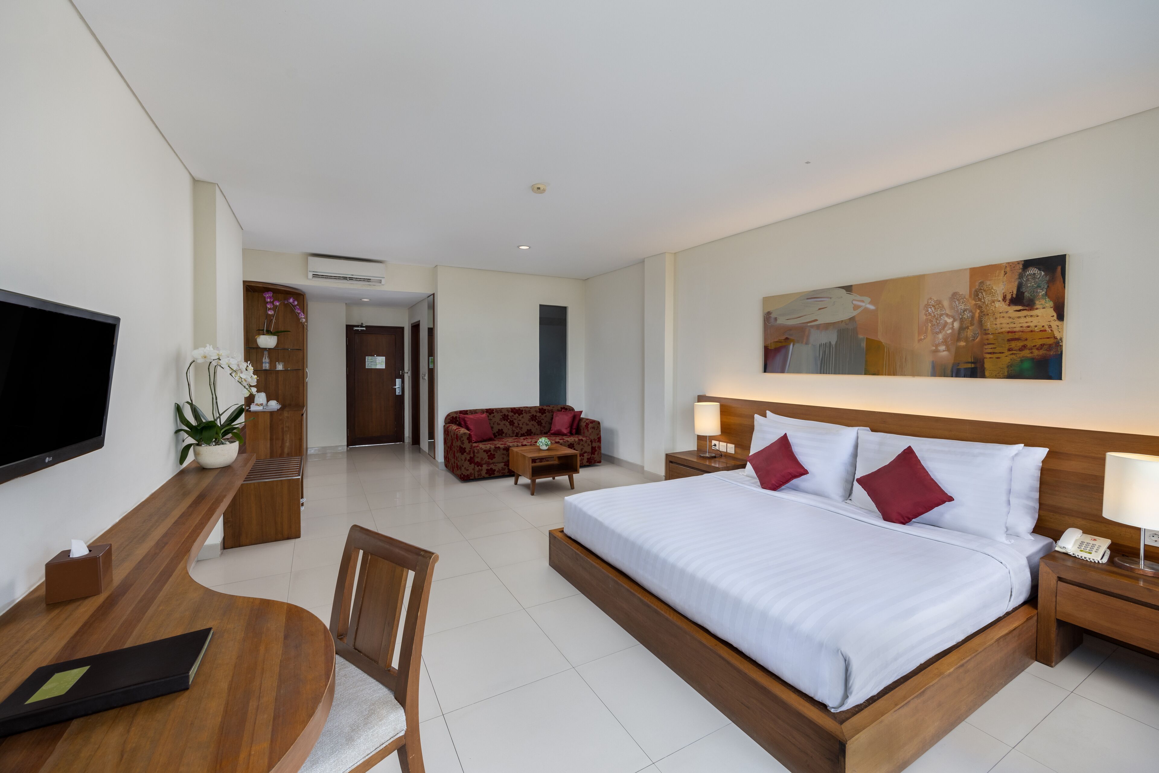 A hotel room with a large bed, a desk with a chair, a sofa, a TV, and a painting on the wall.