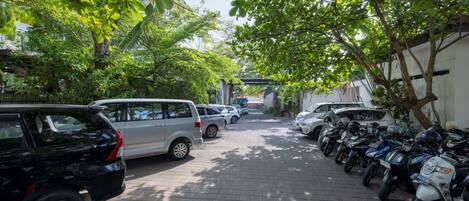 Una calle pavimentada flanqueada por vehículos estacionados, árboles que dan sombra y un edificio al fondo.