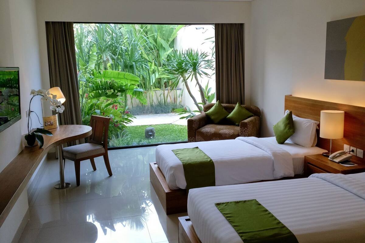Une chambre d’hôtel avec deux lits, un bureau, une chaise et une vue sur un jardin.
