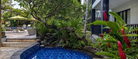 A swimming pool with a tiled edge, surrounded by lush greenery and a wooden deck.