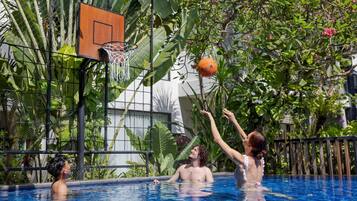 A swimming pool with a basketball hoop and lush tropical plants around it.