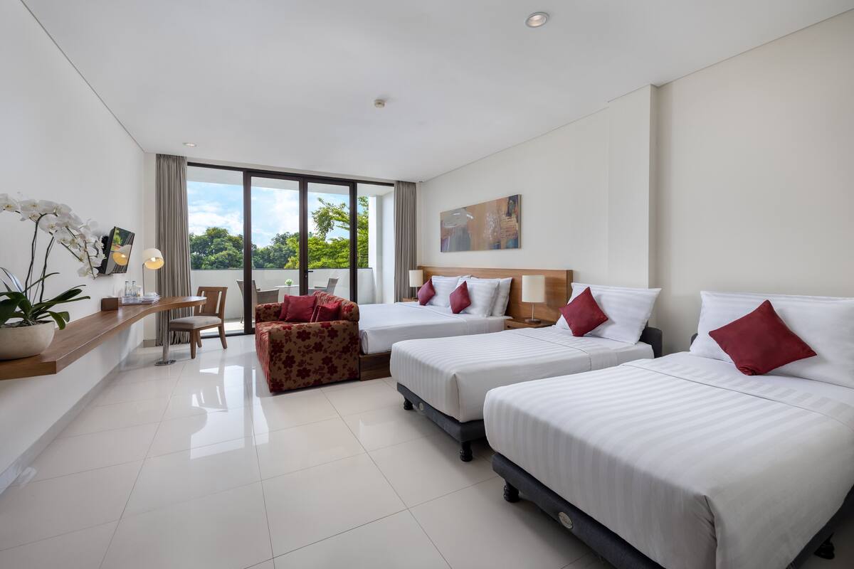 Une chambre d’hôtel avec trois lits, un bureau, une chaise, un canapé et une grande fenêtre donnant sur un paysage verdoyant.