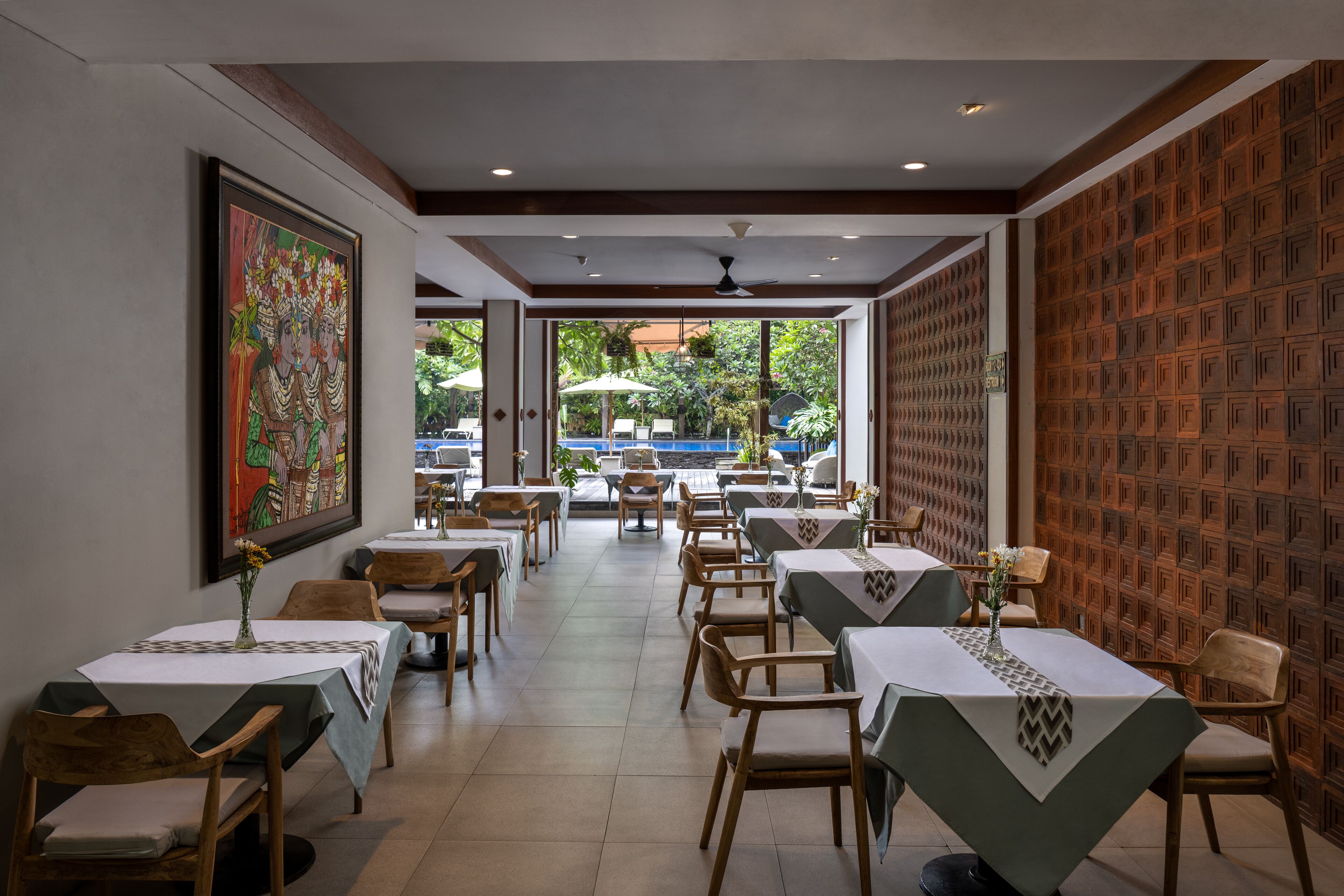 Un restaurant avec des tables et des chaises, un grand tableau accroché au mur et une vue sur l’extérieur.