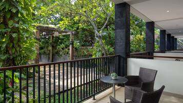 Un balcone con mobili in vimini, un tavolino e vista su un giardino con pergolato e alberi.