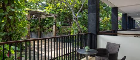 A balcony with wicker furniture, a small table, and a view of a garden with a pergola and trees.