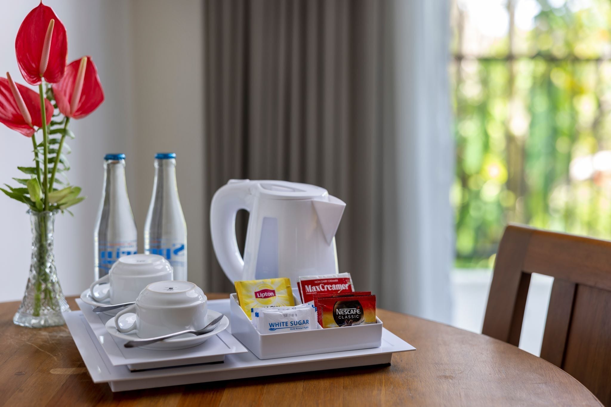 Una bandeja de desayuno con tazas, una tetera y sobres de café sobre una mesa.