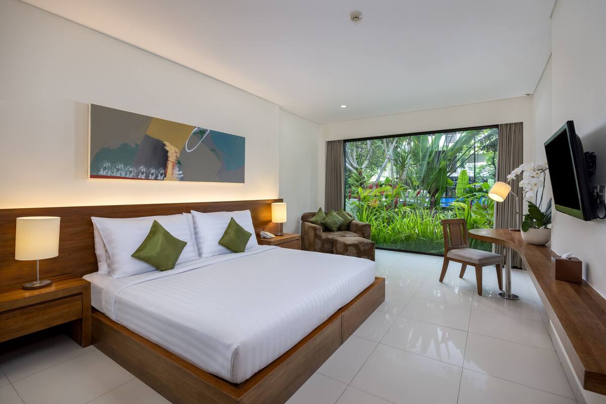 Une chambre d’hôtel moderne, dotée d’un grand lit, d’un bureau et offrant une vue sur la verdure par la fenêtre.