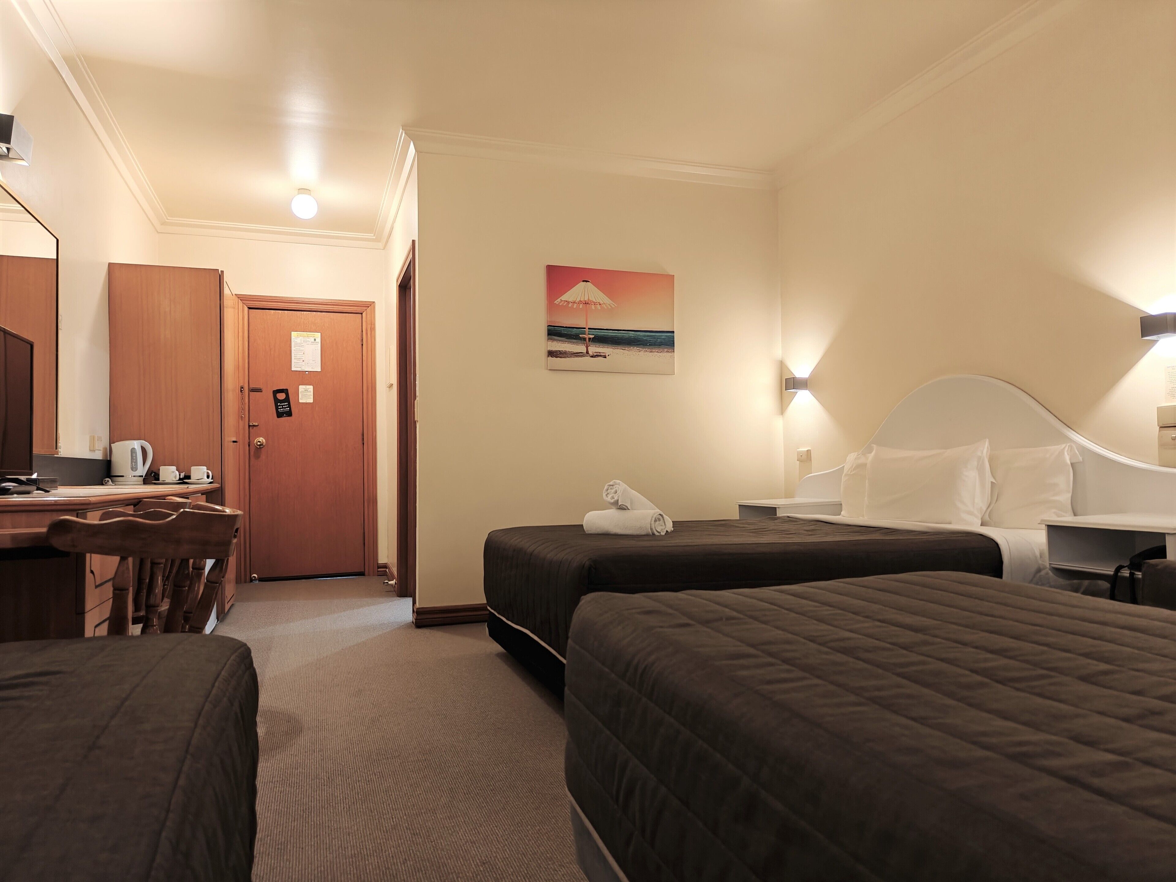 A hotel room with two beds, a desk with a chair, a coffee maker, and a painting on the wall.
