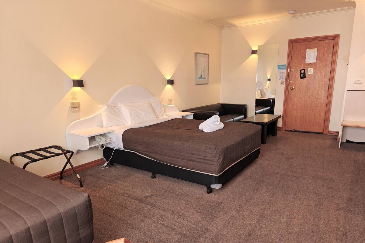 A hotel room with a bed, bedside tables, a desk, a chair, and a wardrobe.