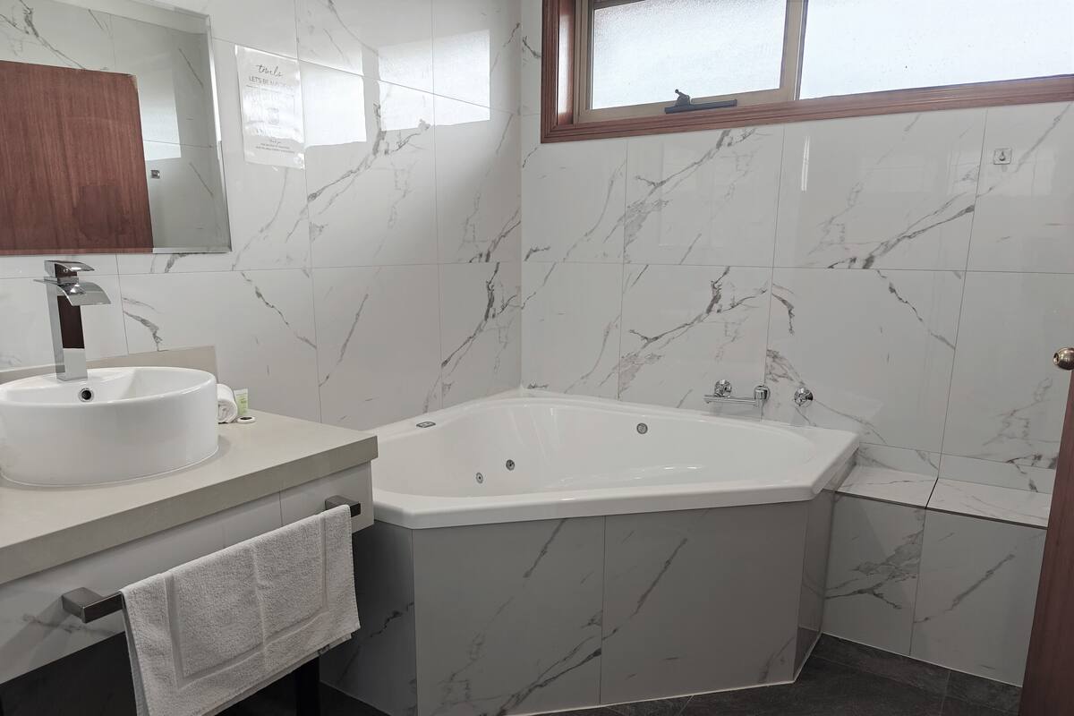 A modern bathroom with a marble wall, a white sink, a bathtub, and a window.