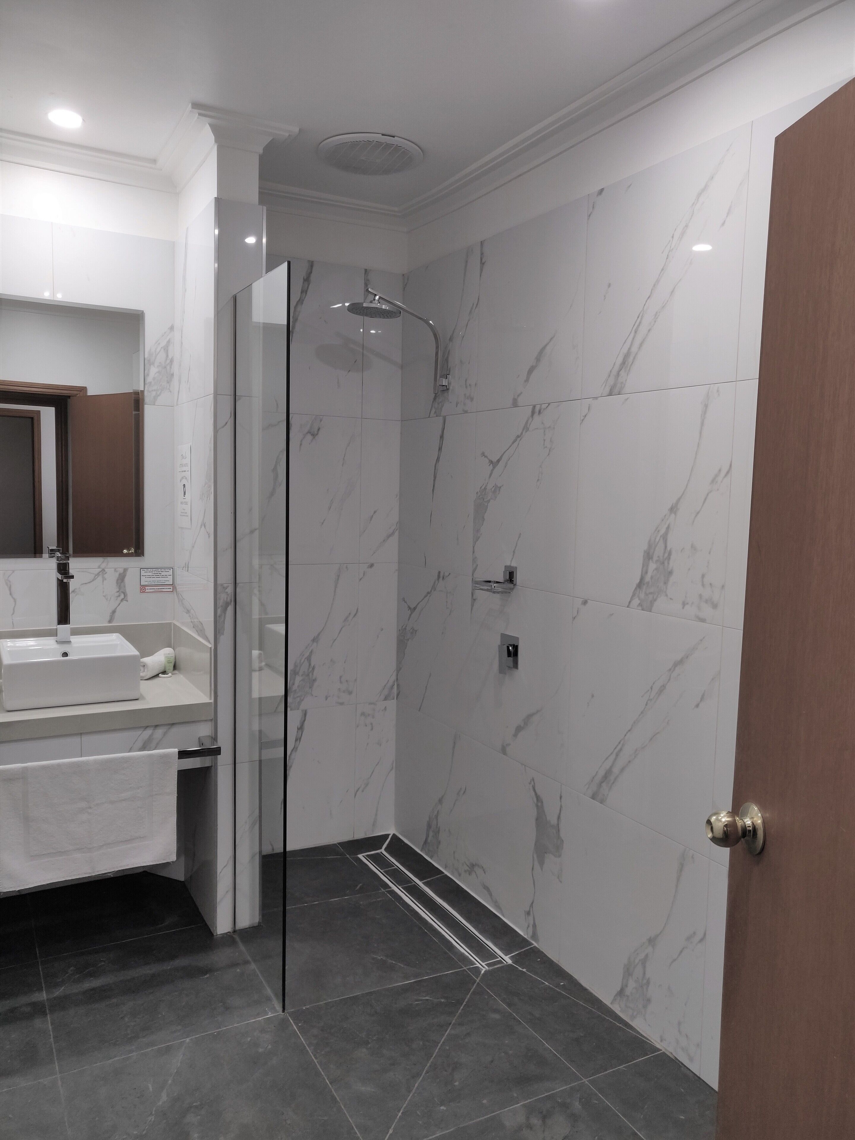 Een moderne badkamer met een douche met glazen wand, een wastafel met spiegel en donkere betegelde vloer.