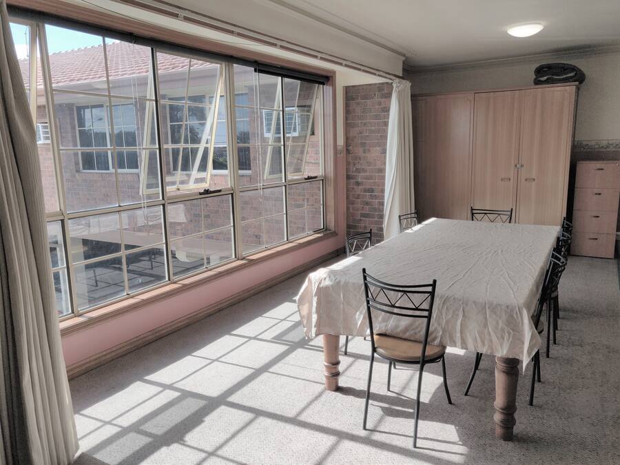 A room with a large window, a dining table with chairs, a wardrobe, and a brick wall.
