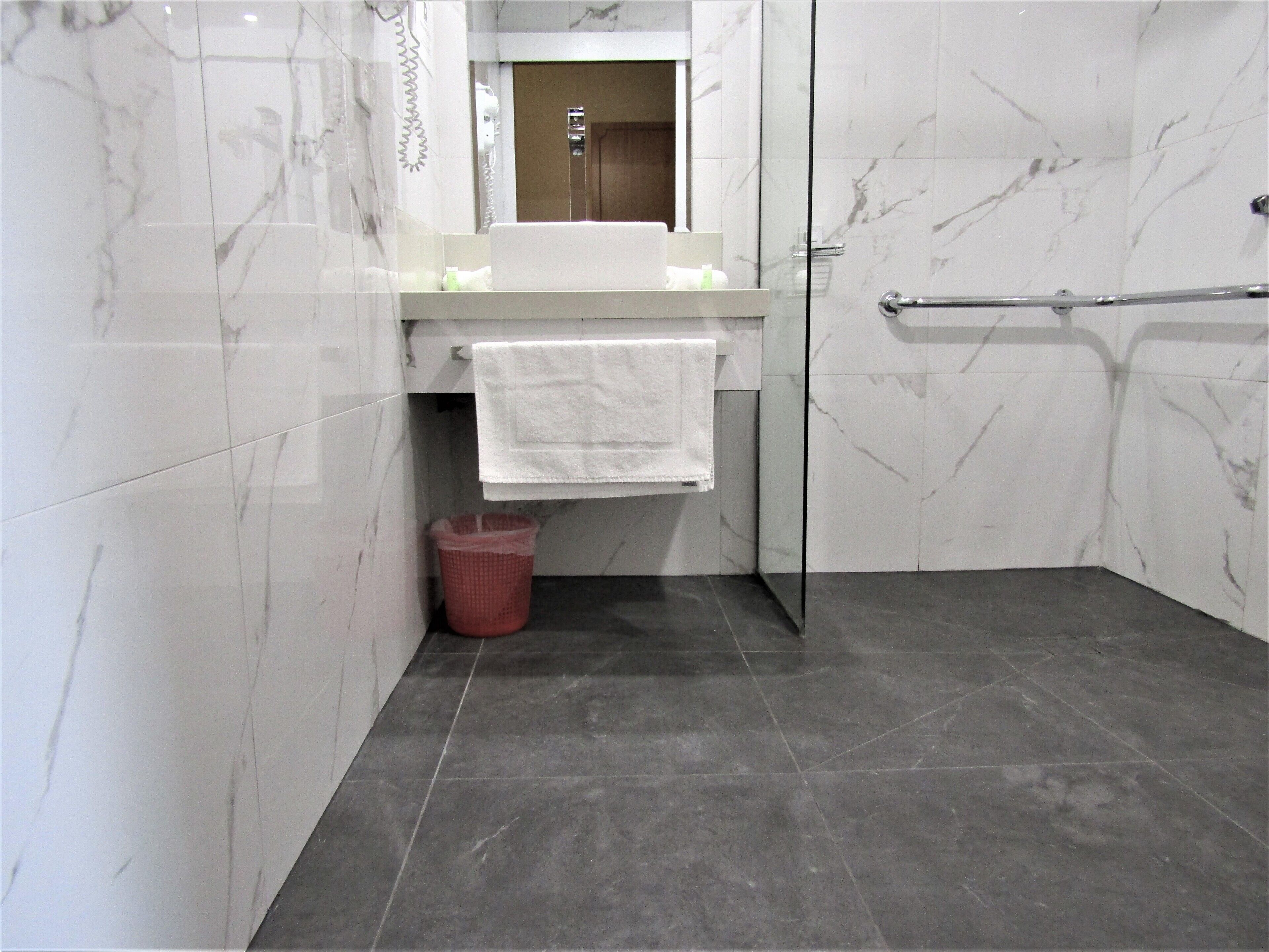A modern bathroom with a glass shower enclosure, a white sink, and a marble-tiled wall.