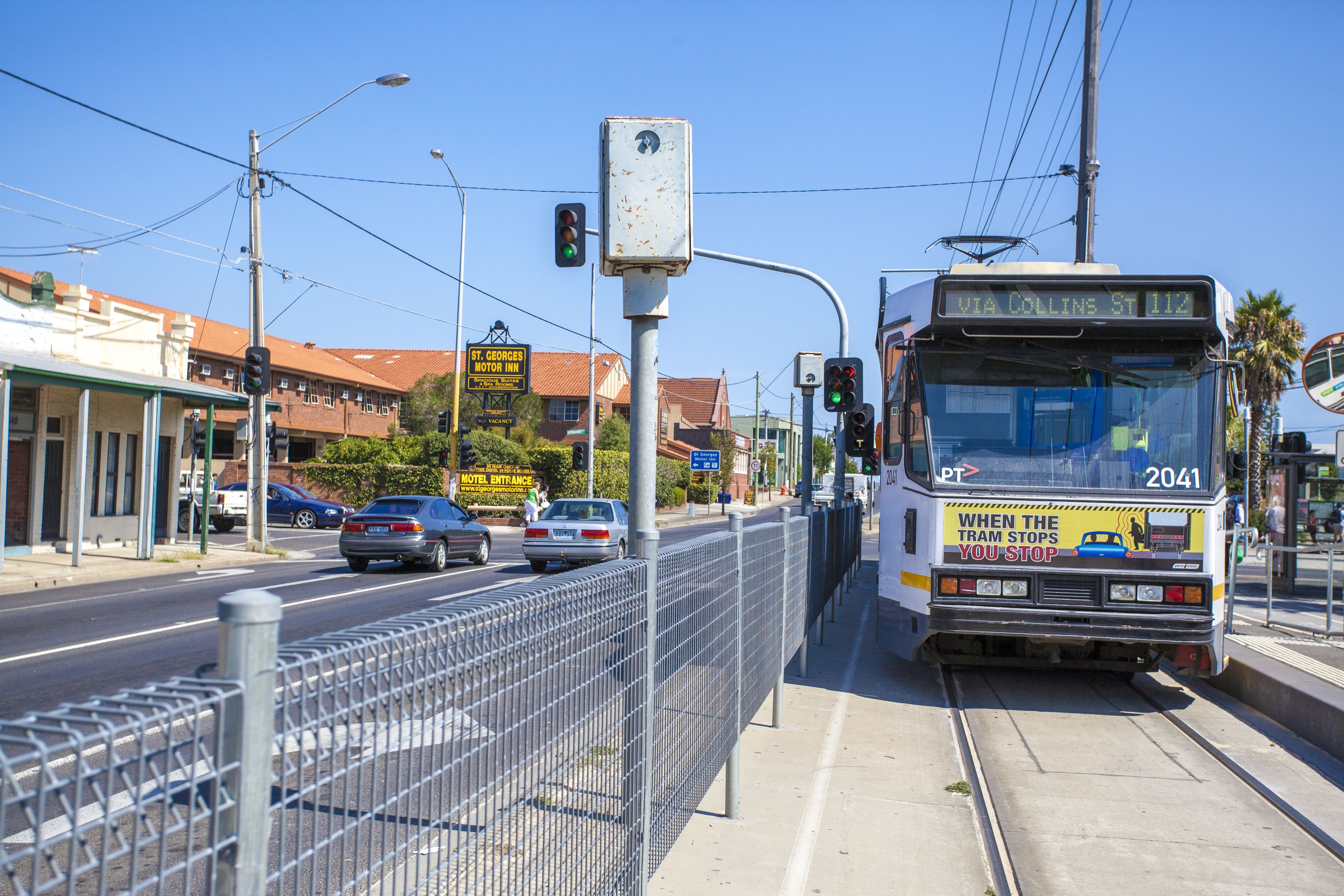 A tram with a sign reading "VIA COLLINS ST 112" and a "MOTEL ENTRANCE" sign in the background.