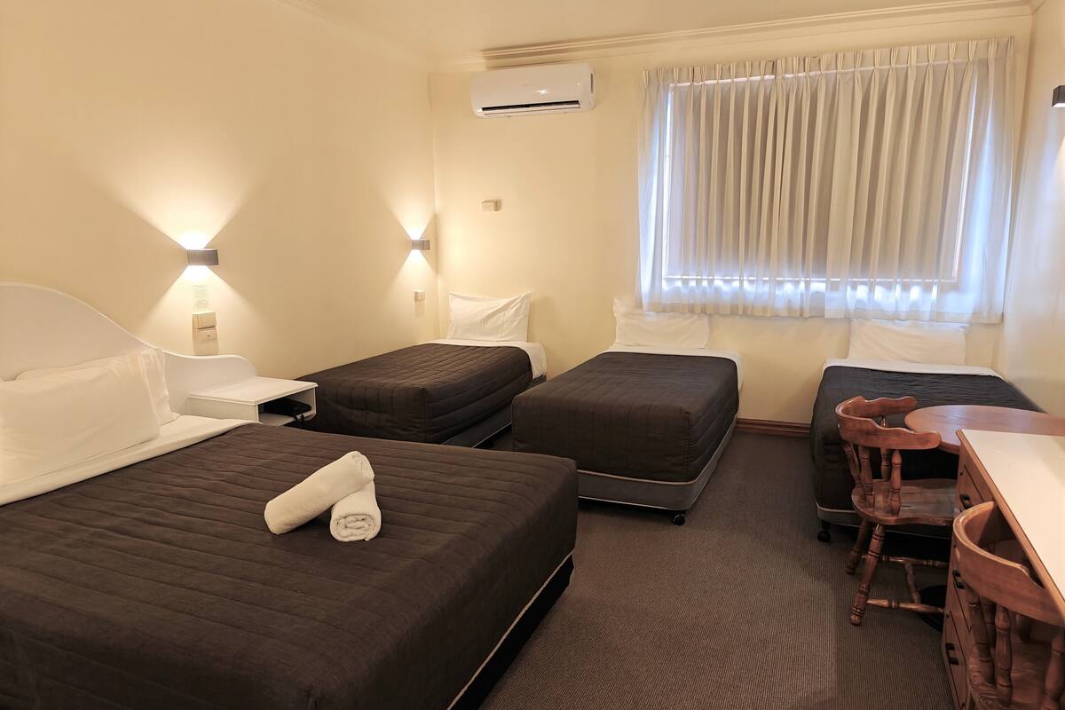 A hotel room with two beds, a desk, a chair, and a window with curtains.
