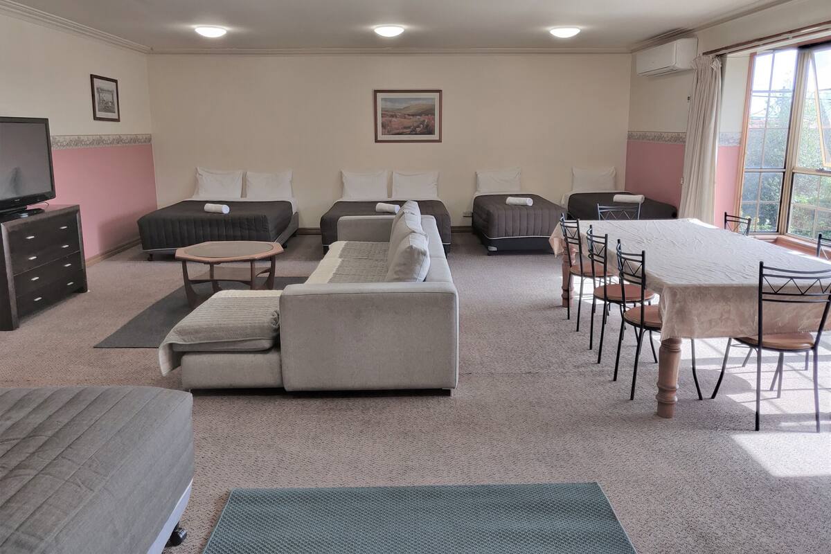 A hotel room with a sofa, two beds, a dining table, and a TV.