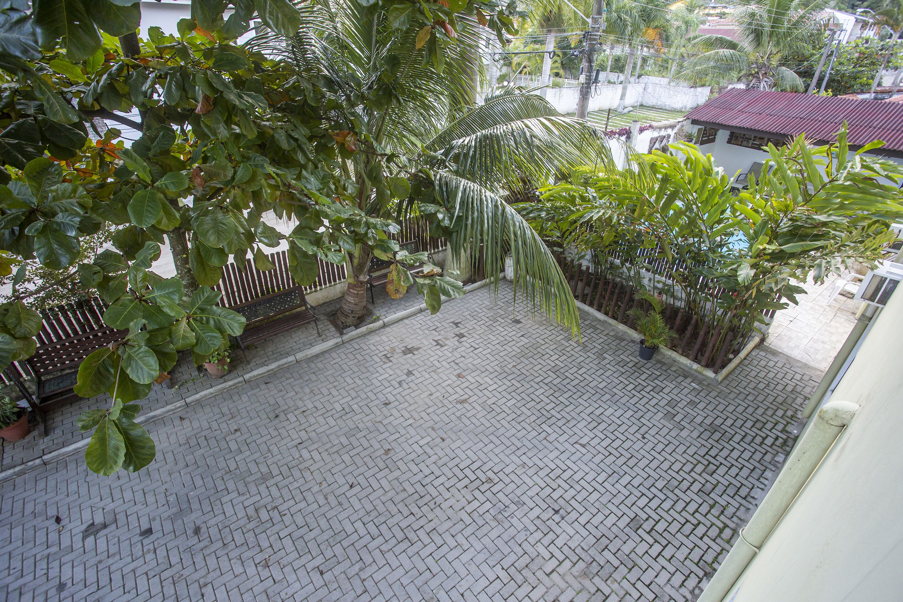 A courtyard with a tiled floor, surrounded by potted plants and a fence.