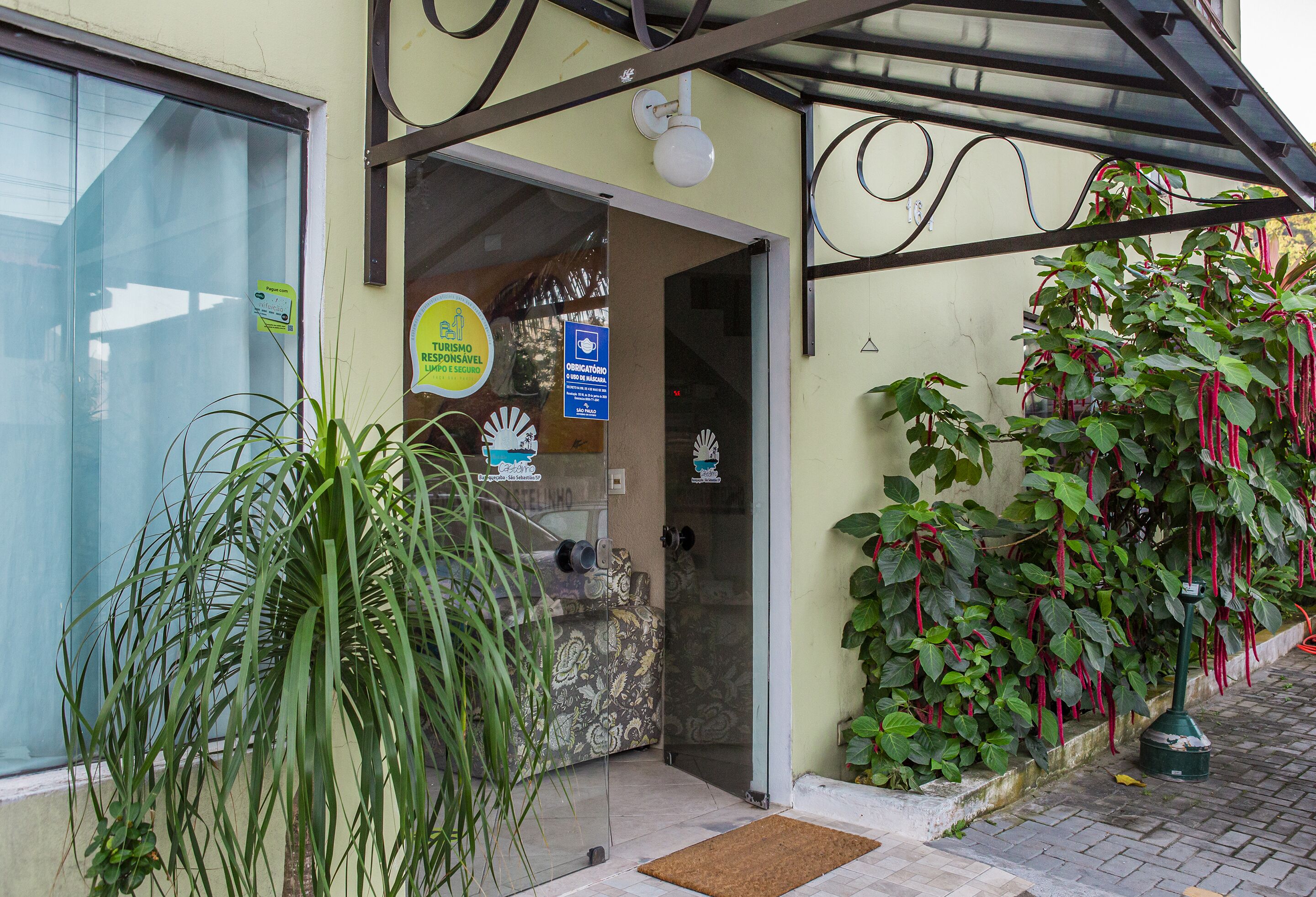 Entrada de un hotel con puerta de vidrio, recepción a la vista y una planta en maceta.