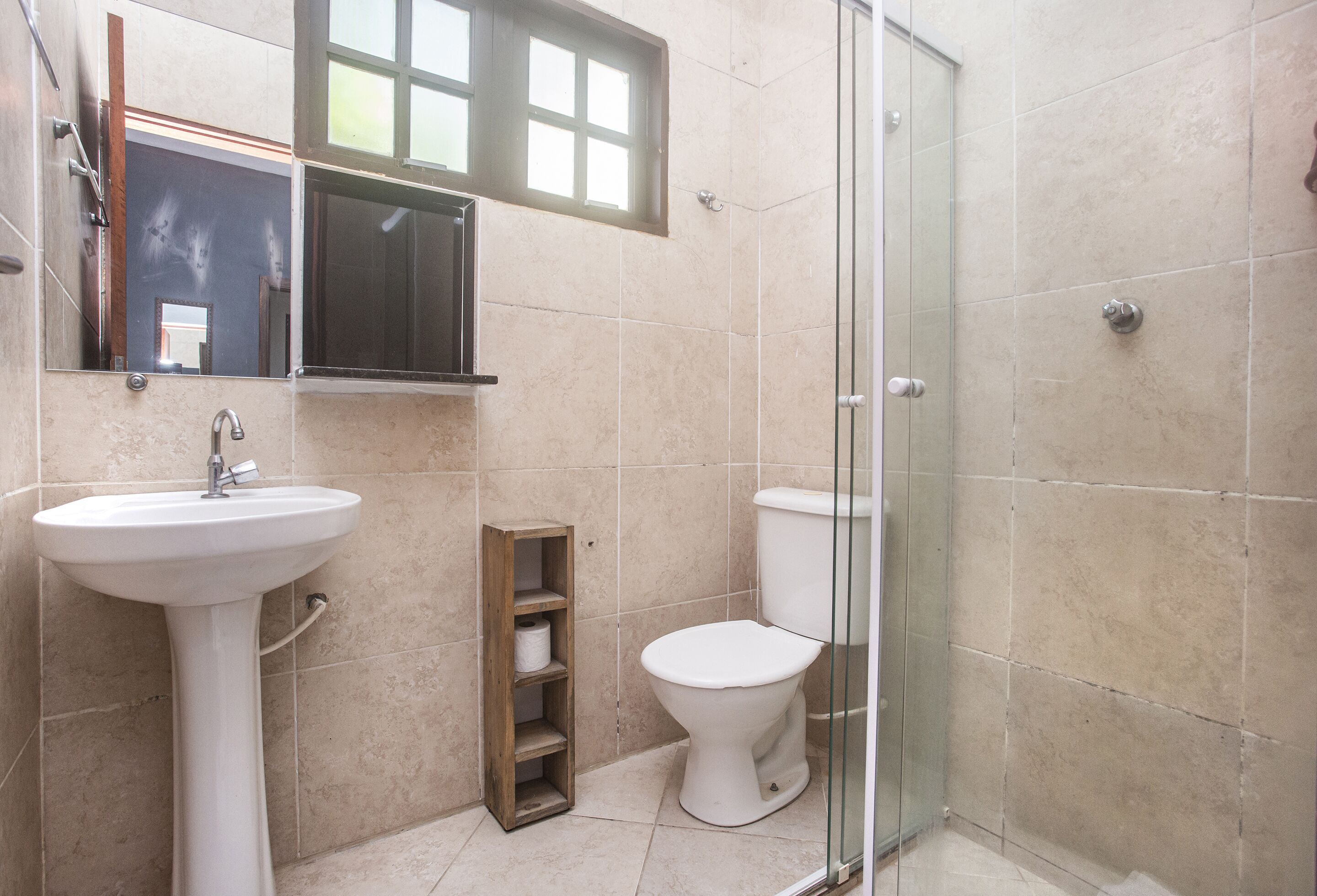 Een badkamer met een wastafel op een voetstuk, toilet en een douchecabine met glazen wanden.