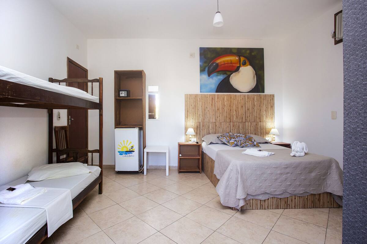 Ein Zimmer mit Etagenbett, einem Einzelbett, einem Kühlschrank, einem Nachttisch, einer Lampe und einem Bild eines Tukan.