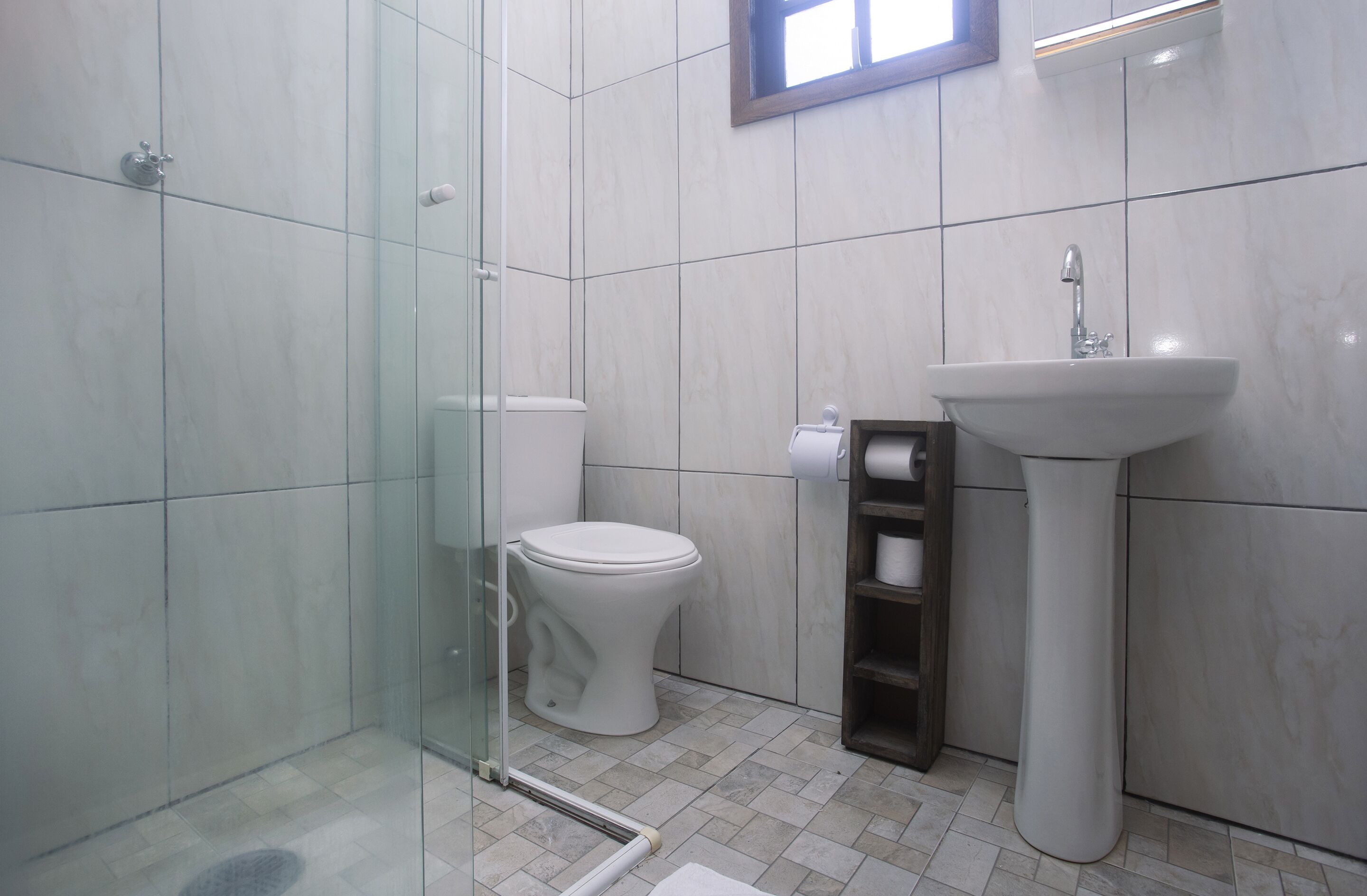 A modern bathroom with a glass shower enclosure, a white toilet, and a pedestal sink.