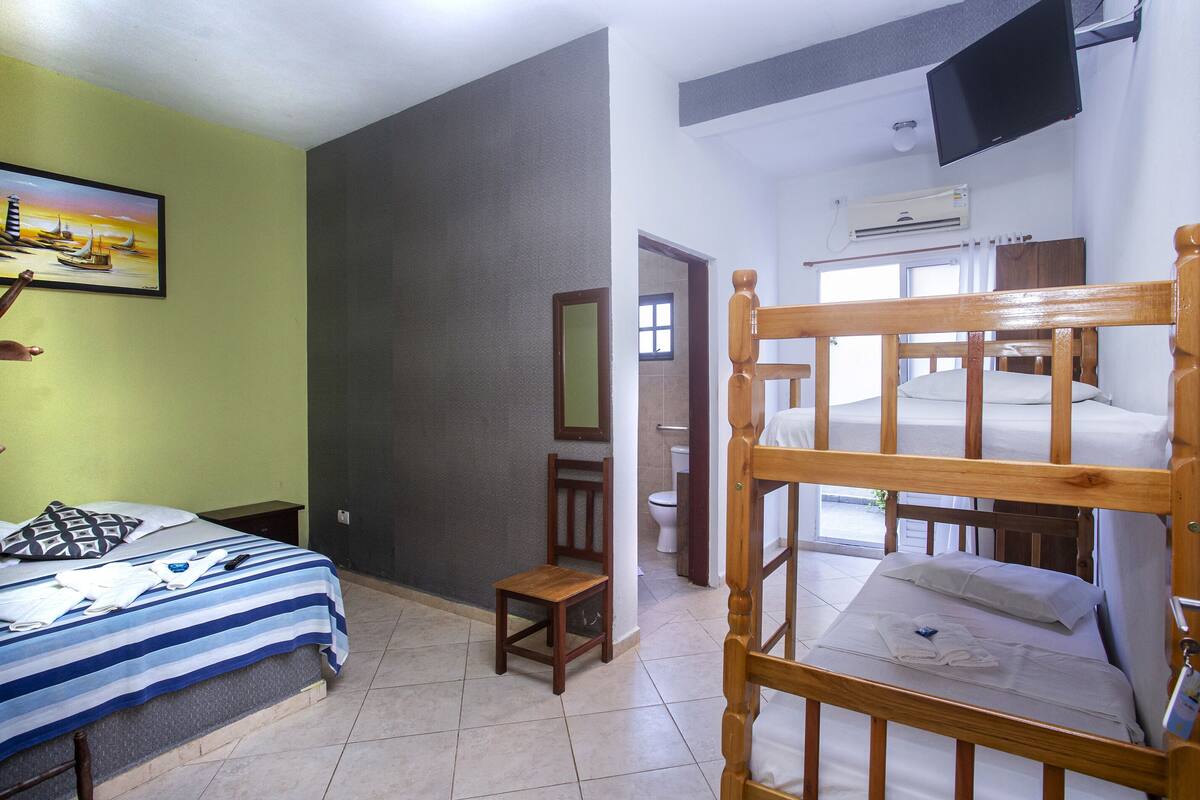 Ein Zimmer mit einem Bett, einem Sessel, einem kleinen Tisch, einem Fernseher und einer Klimaanlage.