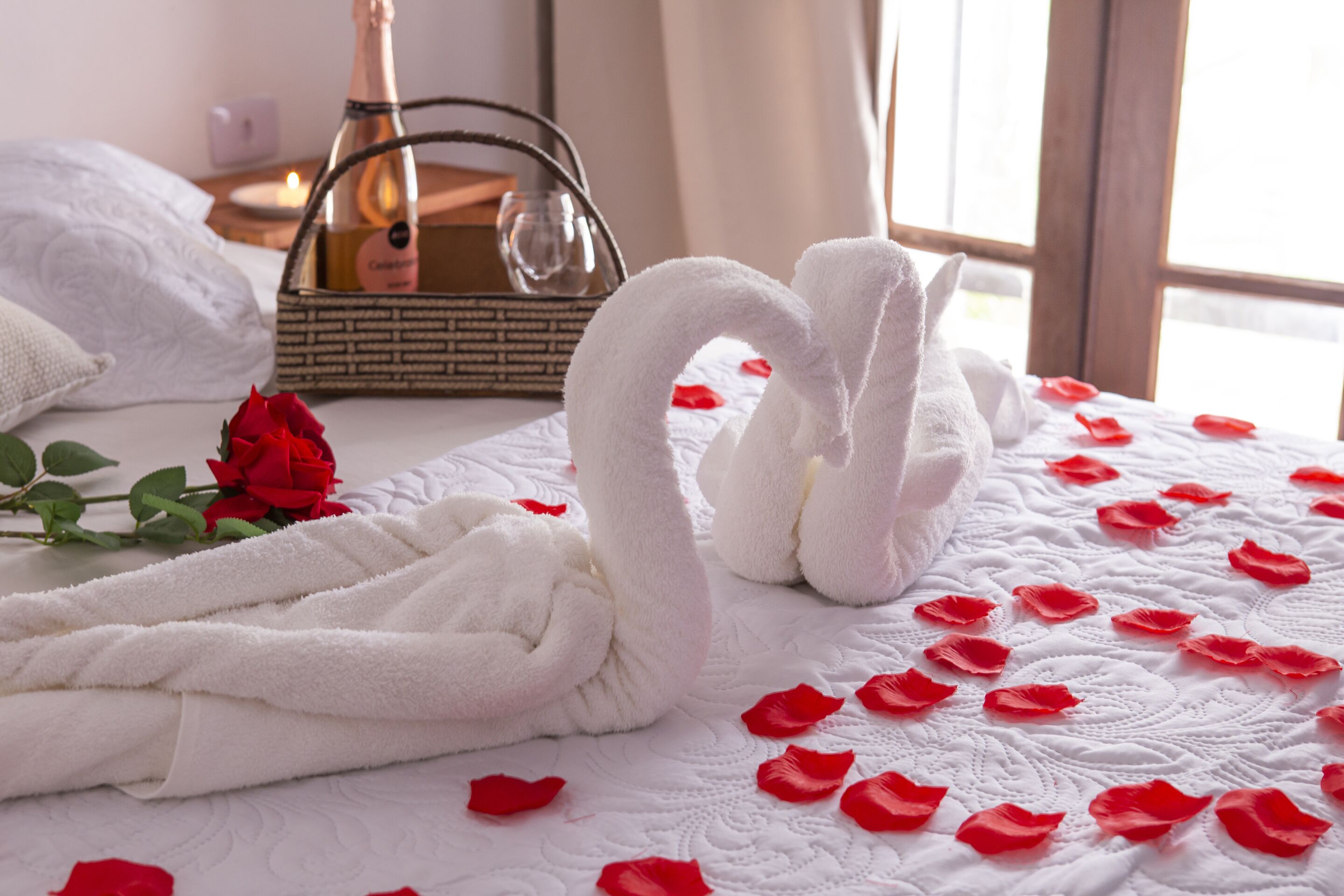 Ein Bett mit weißer Bettdecke, ein Strauß roter Rosen und eine zu einem Schwan geformte Handtuch-Arrangement.