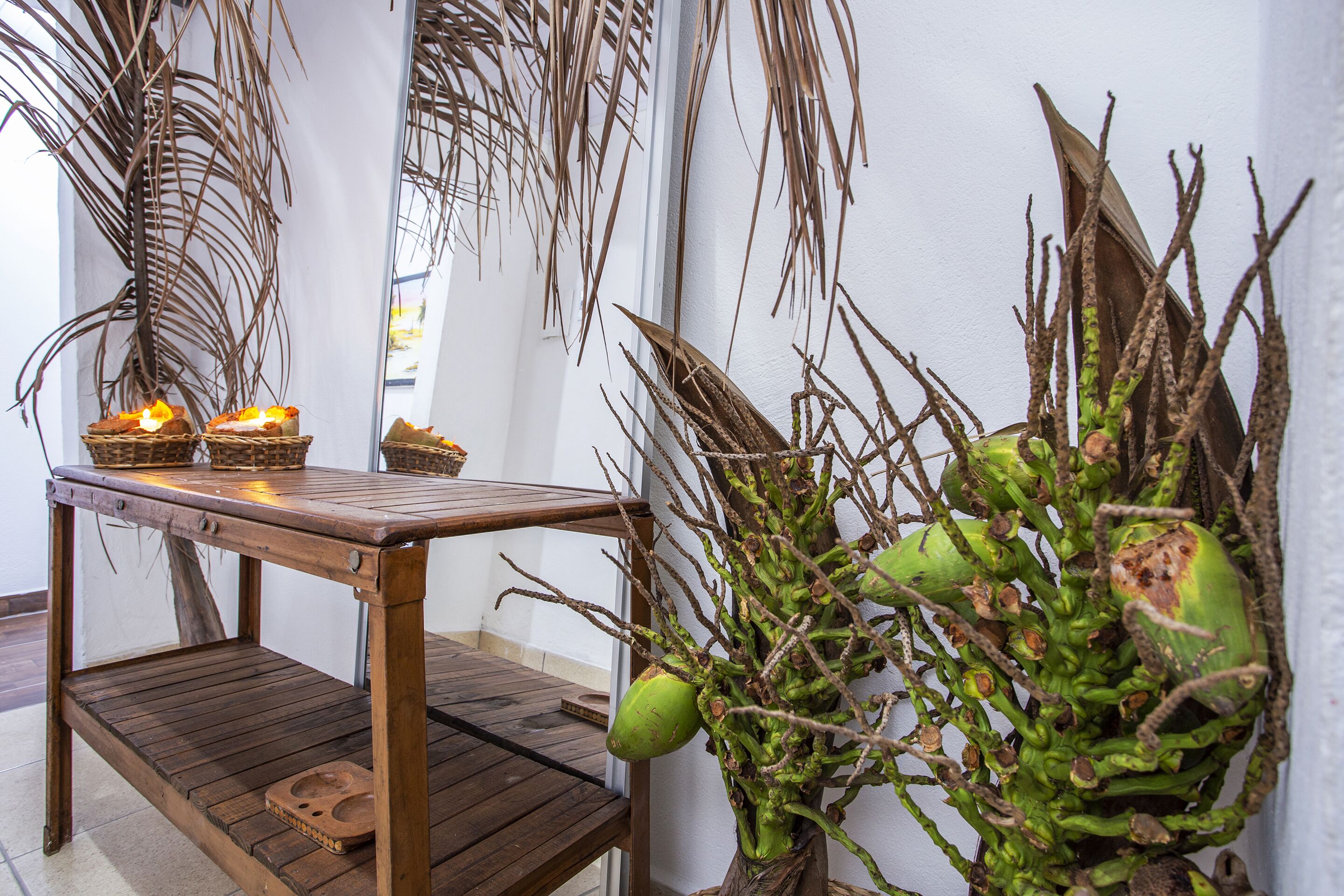 A wooden table with baskets and candles, a potted plant with green leaves, and a wall with a window.