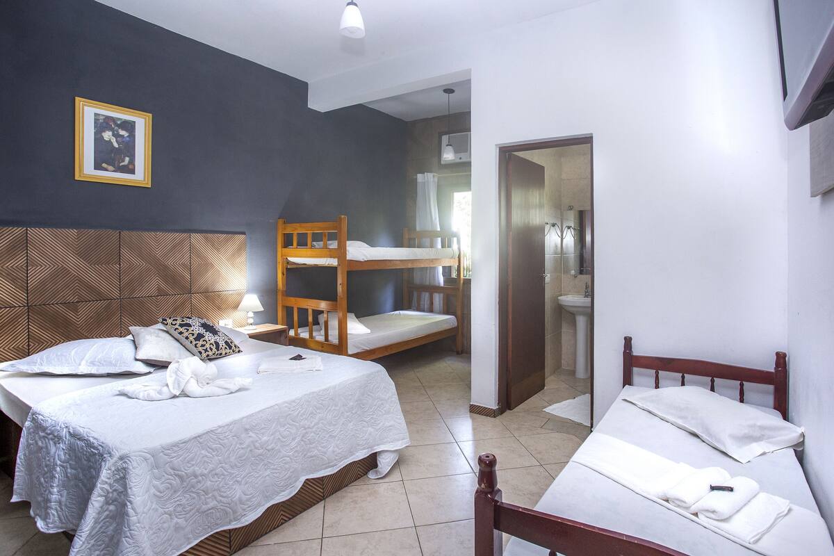 Ein Hotelzimmer mit zwei Betten, einem Etagenbett, einem Badezimmer mit Dusche und einem gerahmten Bild an der Wand.