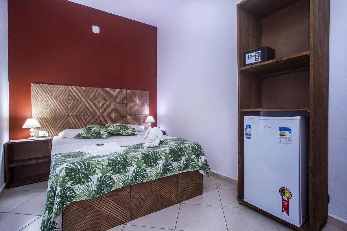 Ein Hotelzimmer mit Bett, Nachttischen, einem Holz-Kopfteil, einem weißen Kühlschrank und einer roten Wand.
