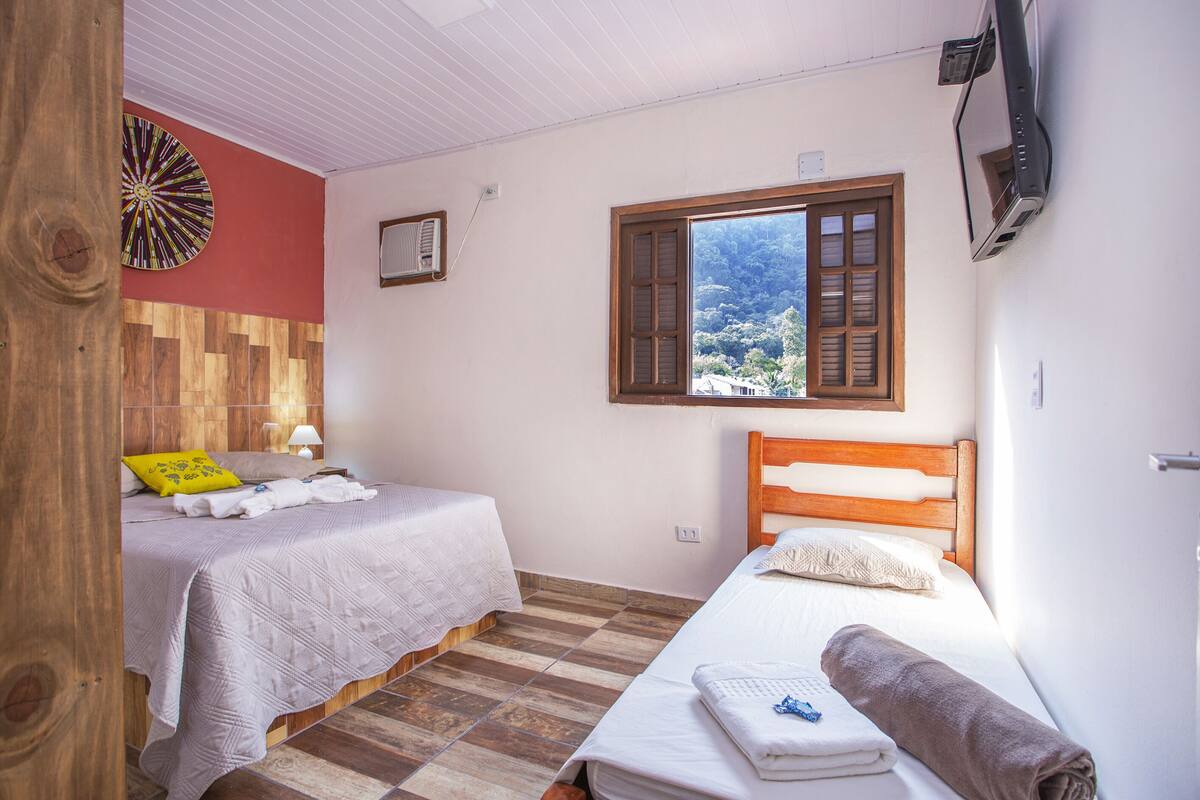 Ein Schlafzimmer mit zwei Betten, einem Holz-Kopfteil, einem Fenster mit Aussicht, einer Dartscheibe und einem Fernseher.