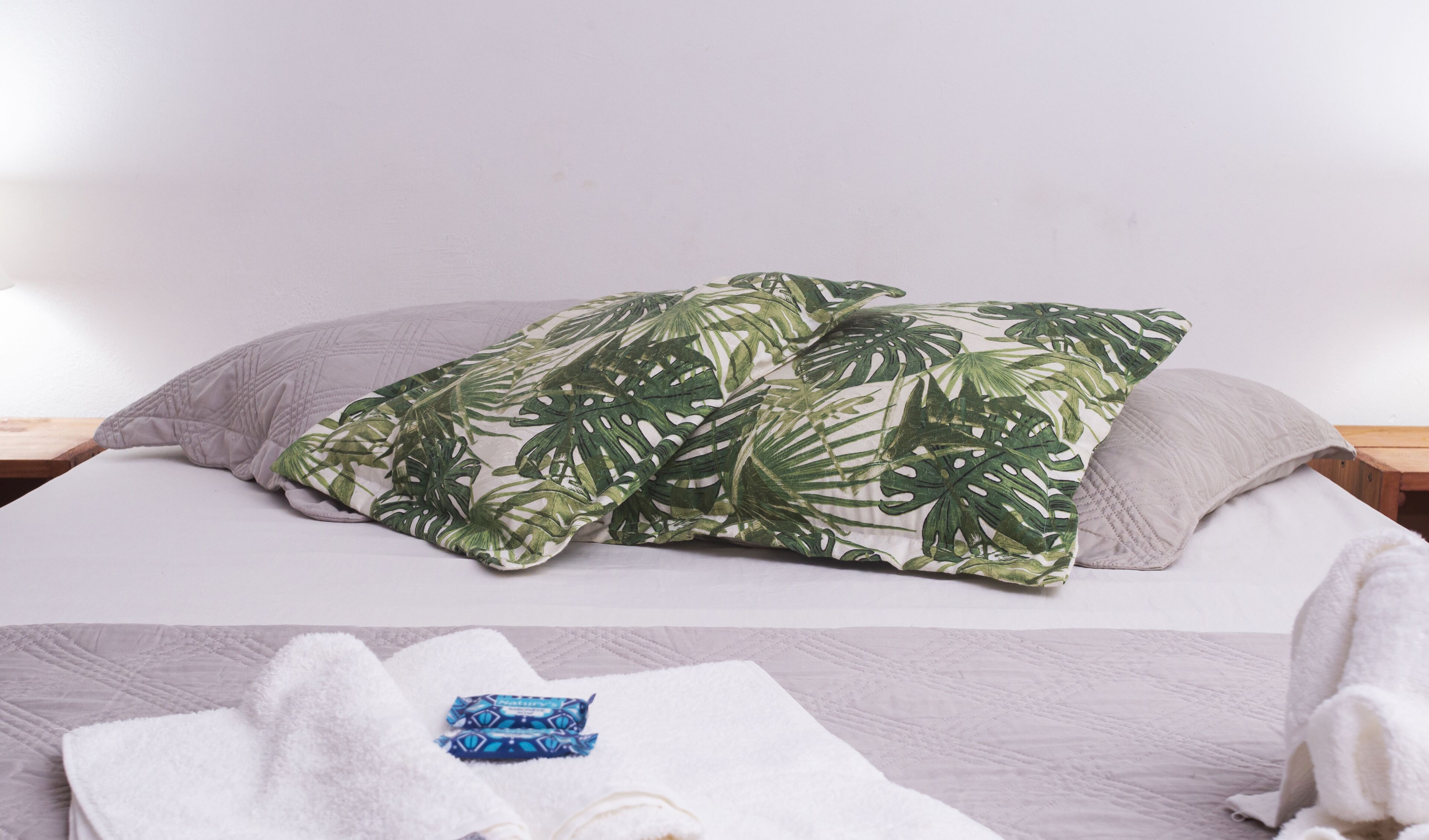Uma cama com um cobertor estampado com folhagens tropicais, uma toalha branca e uma toalha azul sobre a cama.