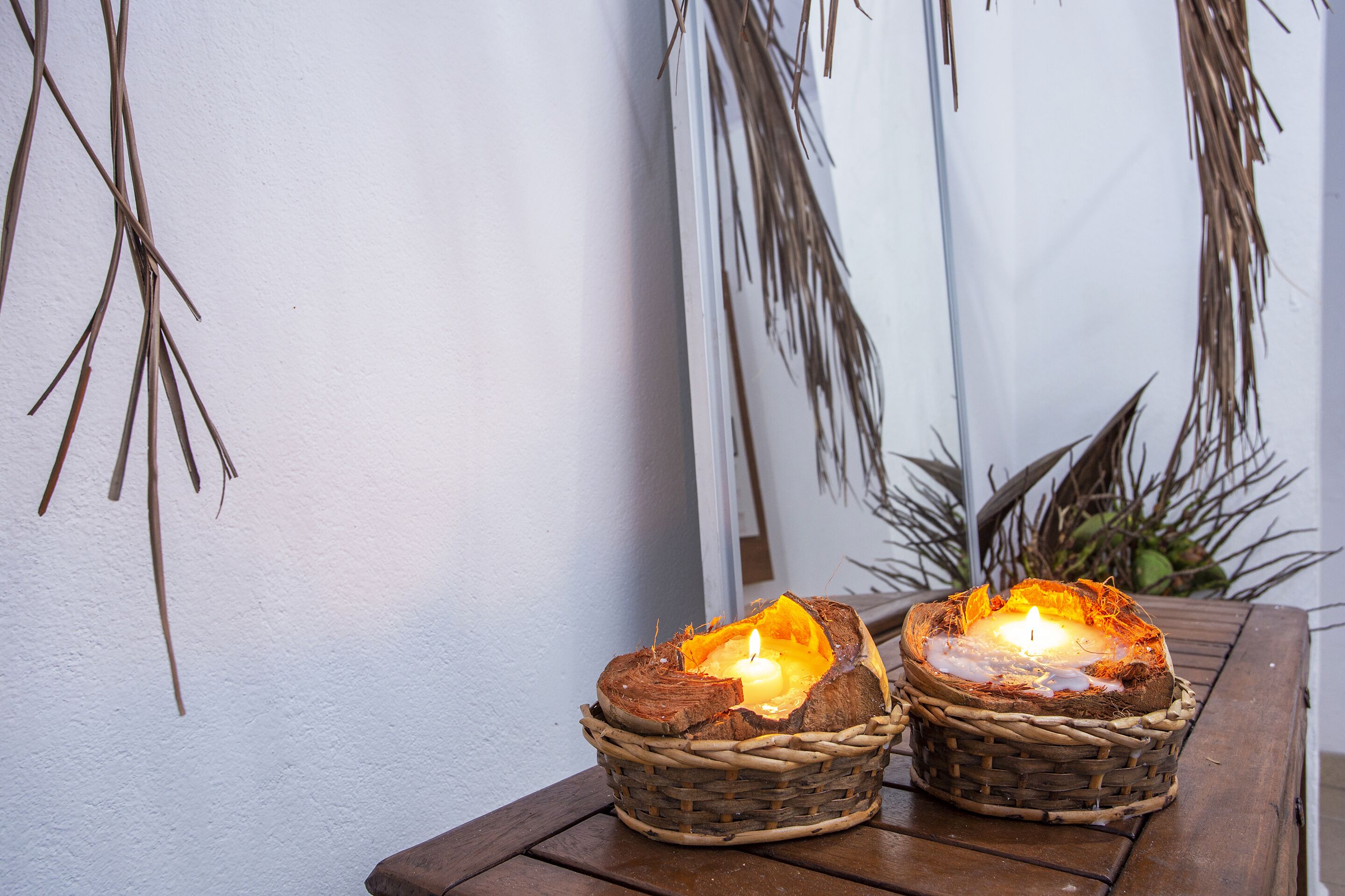 Dos velas encendidas en cestas de mimbre sobre una mesa de madera.