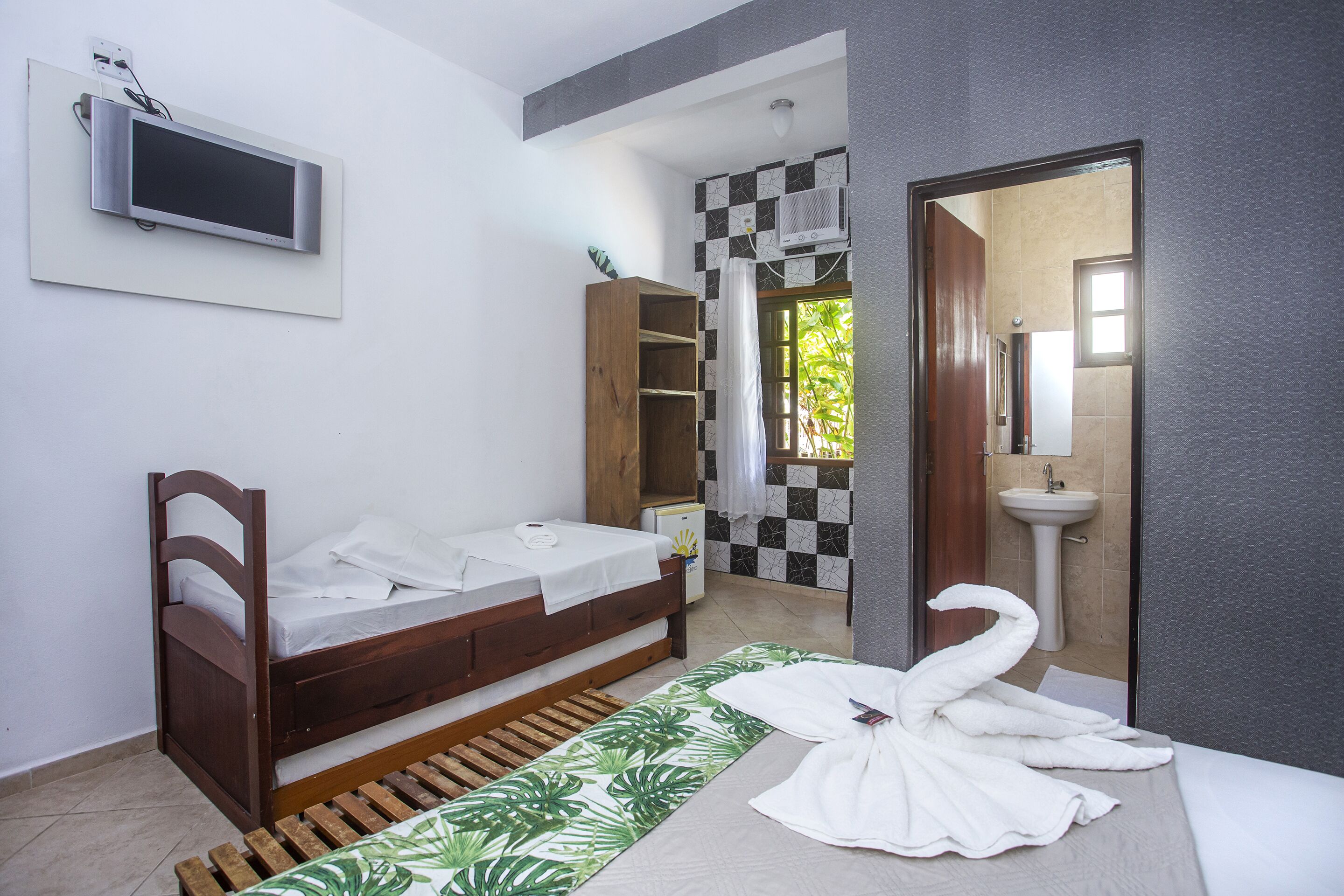 A bedroom with a bed, a TV, a wardrobe, a bathroom with a sink, and a shower.