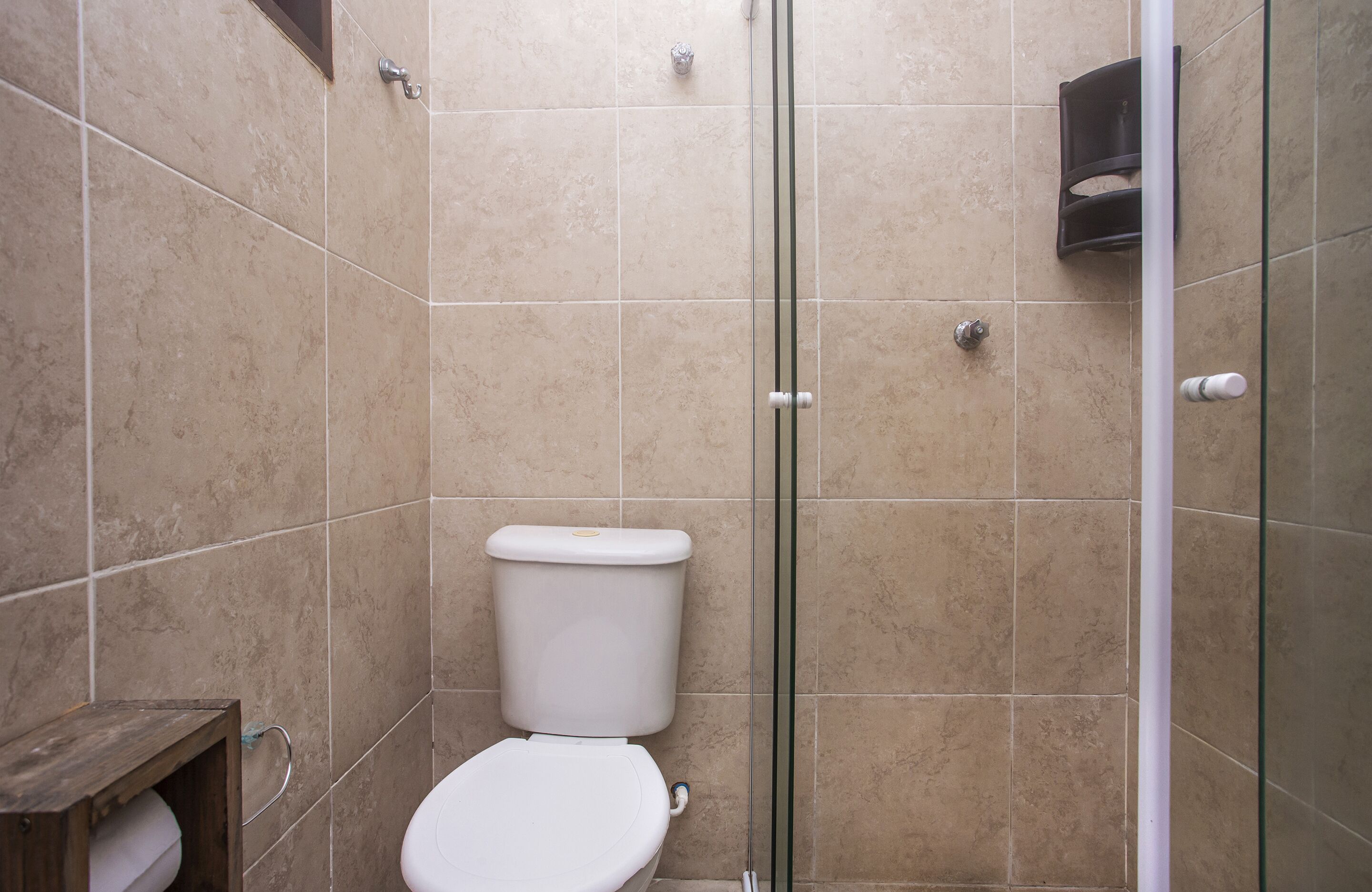 Un baño con inodoro, cabina de ducha de vidrio y paredes con azulejos color crema.