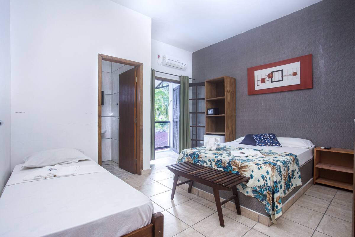 Ein Schlafzimmer mit zwei Betten, einer Holzbank, einem an der Wand befestigten Regal und einer Tür zu einem Außenbereich.