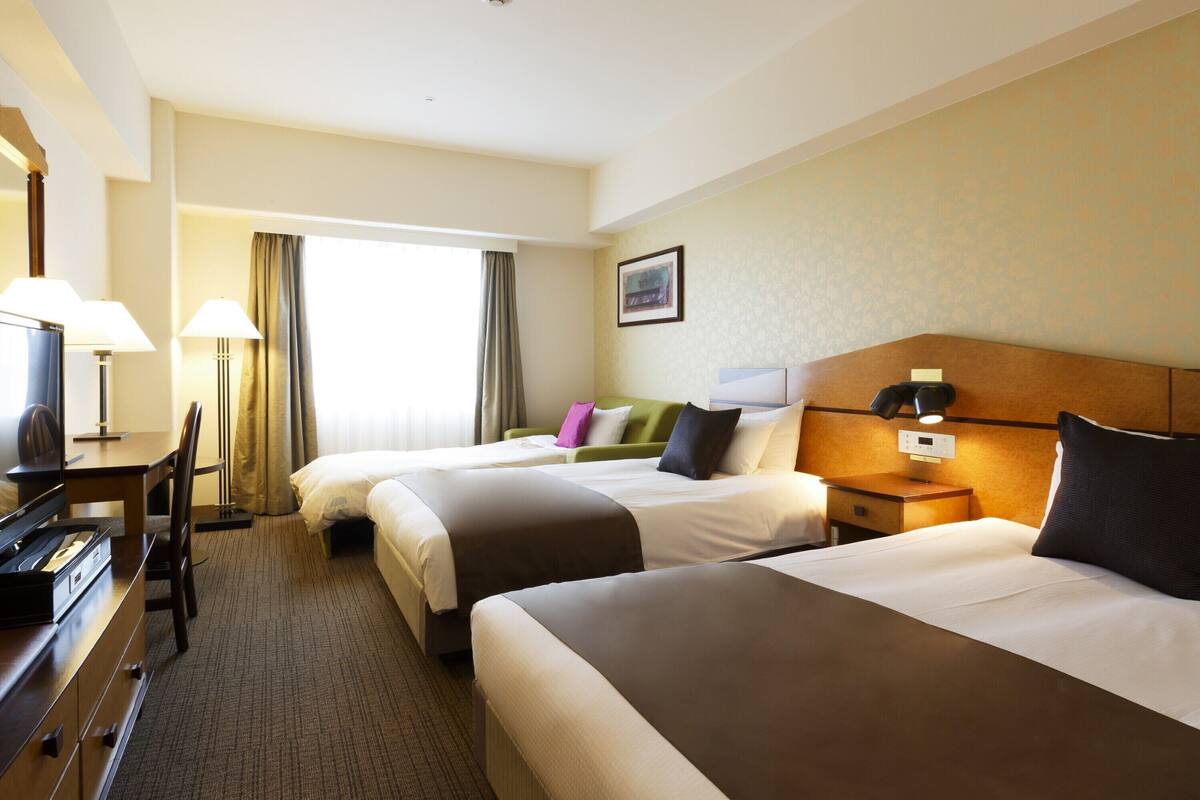 A hotel room with two beds, a desk with a computer, a lamp, and a window with curtains.