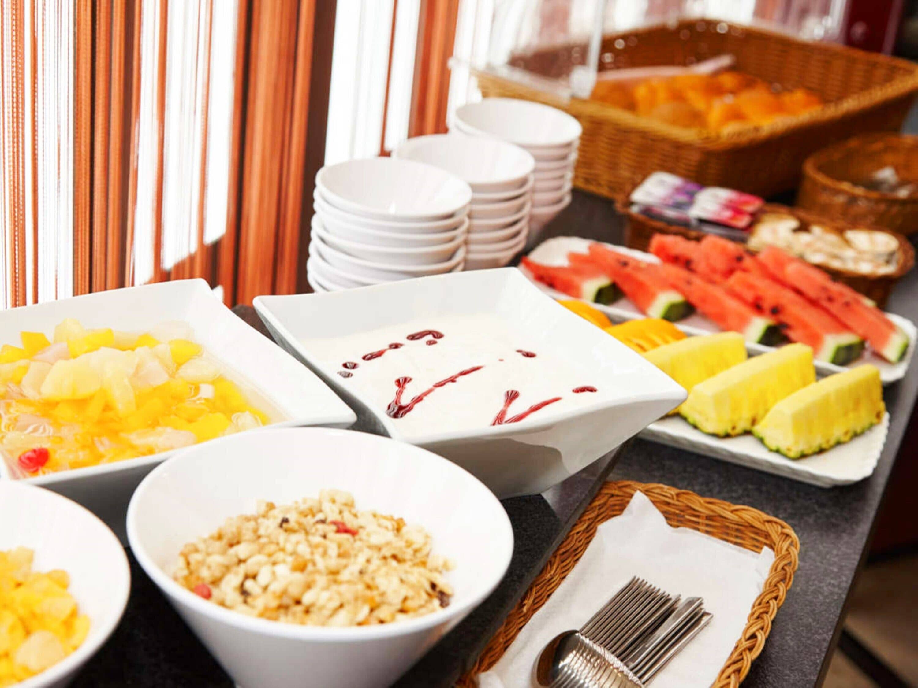 A buffet with various food items including fruits, a bowl of cereal, and a basket of bread.